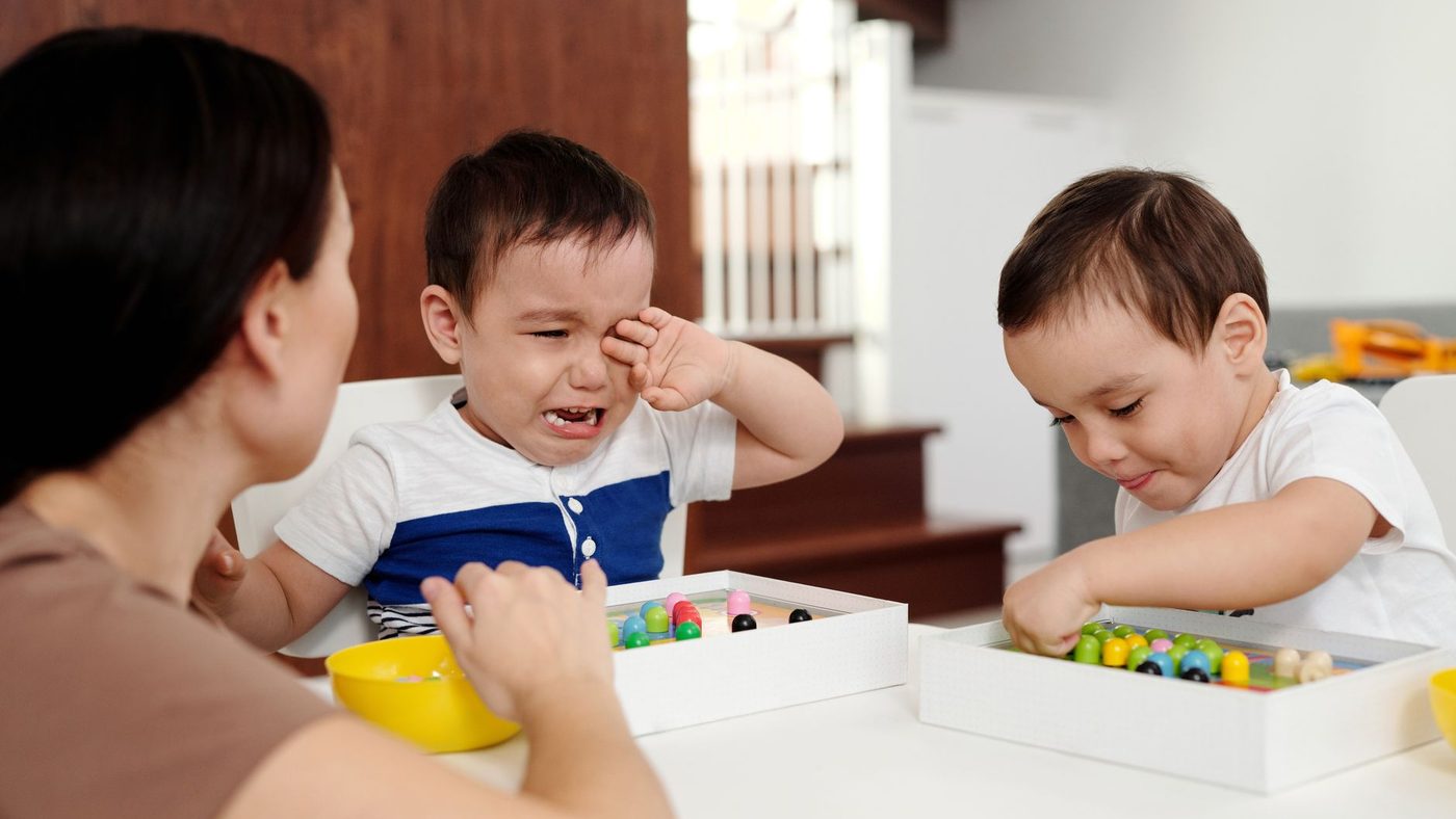 Une mère console un petit garçon en larmes pendant que son frère joue à côté