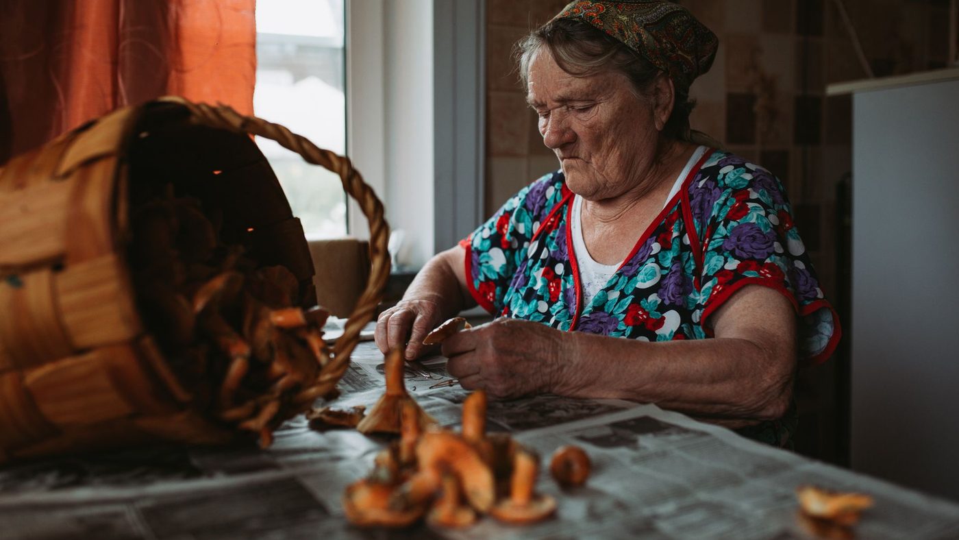 Une femme âgée trie des champignons sur une table, à côté d'un panier renversé