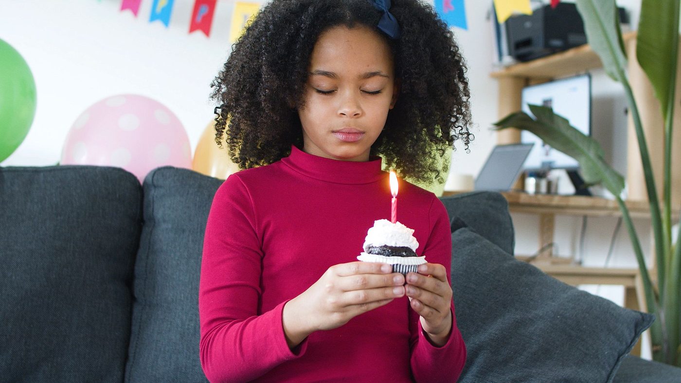 Une fillette tient devant elle un petit gâteau surmonté d'une bougie allumée