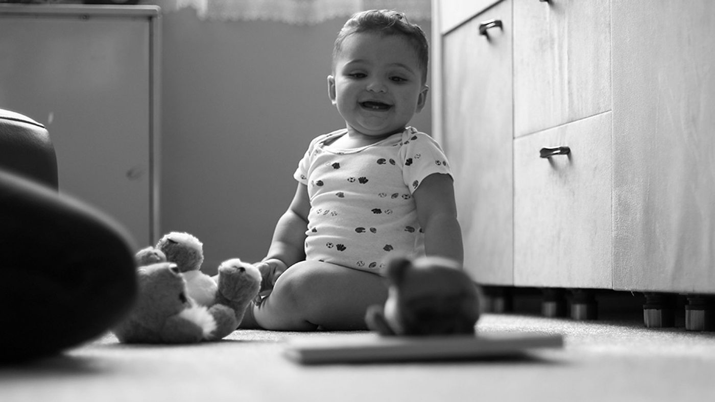 Bébé assis seul au sol dans une chambre, quelques jouets autour de lui