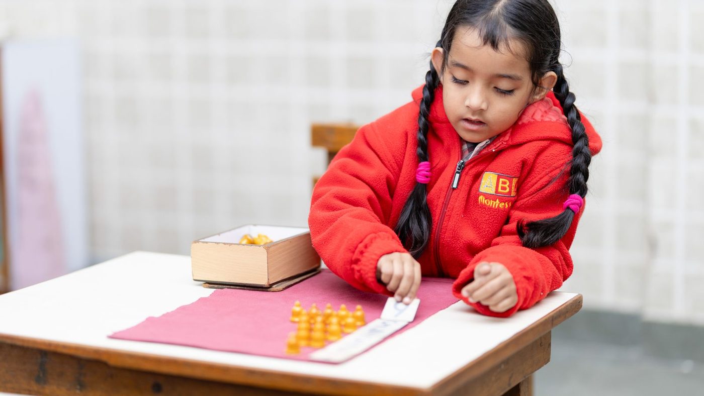 Enfant qui aligne des barrettes de perles dorées sur sa table