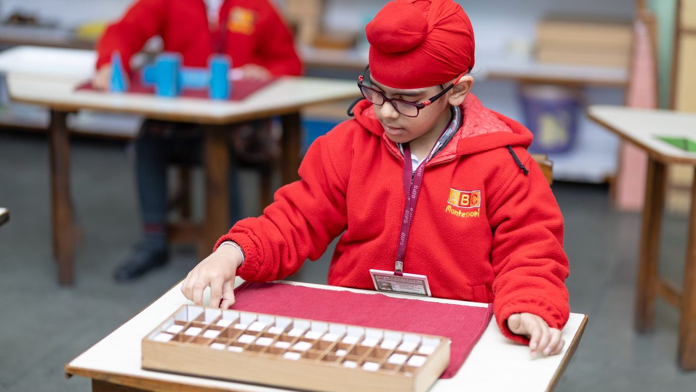Enfant assis à sa table dans une classe Montessori, un bloc de cylindres devant lui