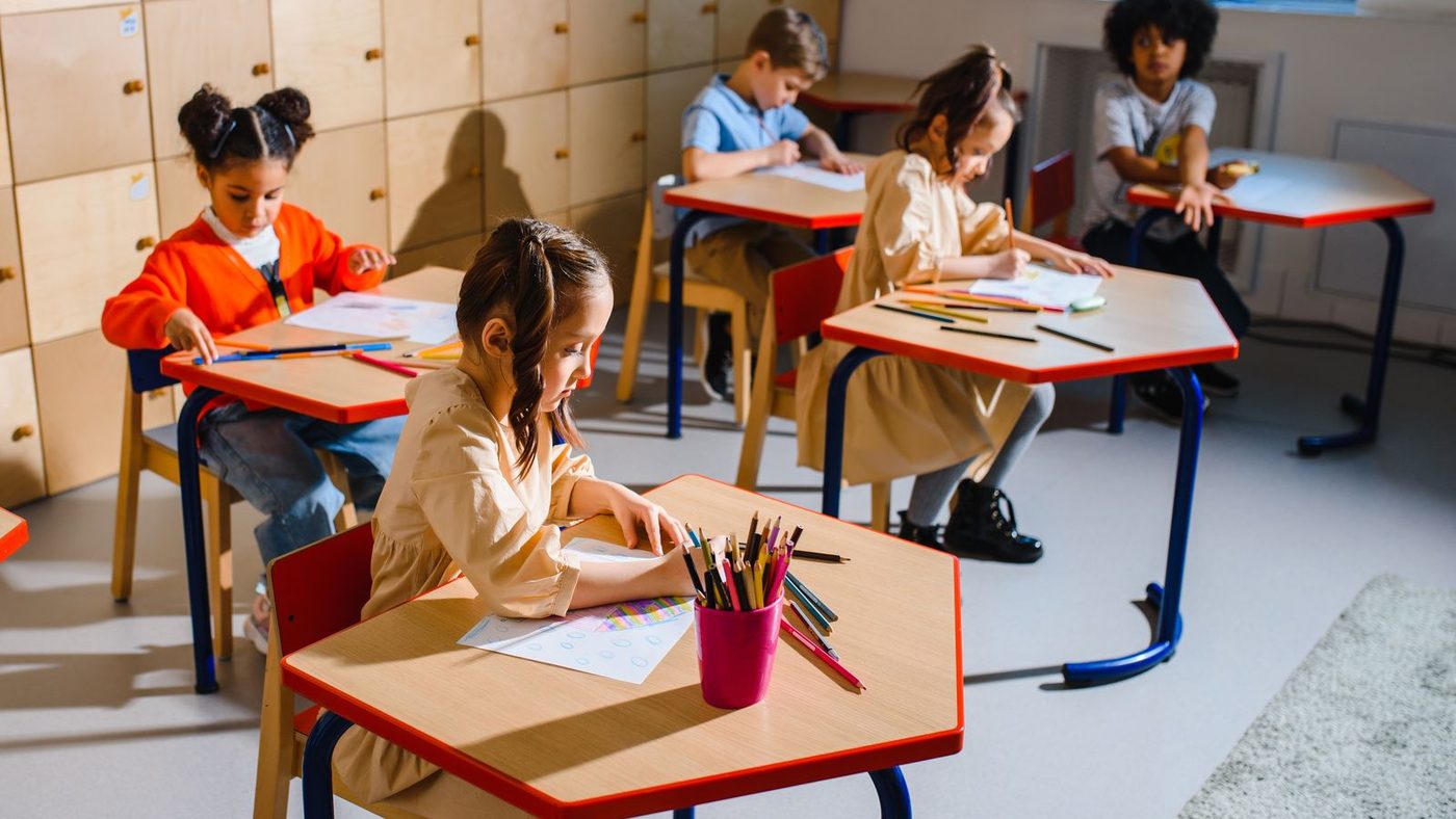Classe de maternelle organisée en tables d'ateliers, les enfants au travail par petits groupes