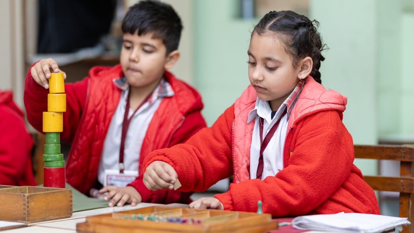 Deux enfants côte à côte dans une classe Montessori, chacun sur son propre matériel