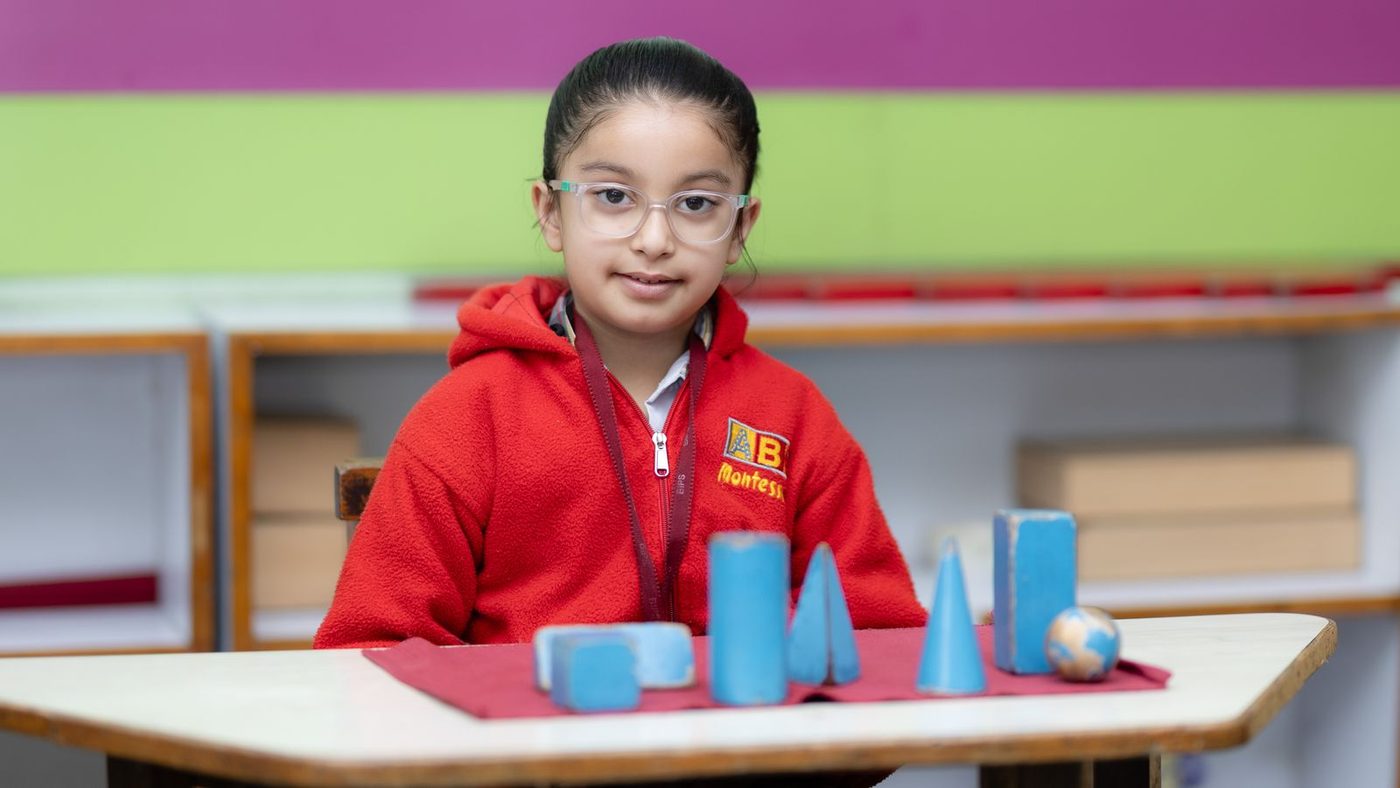 Enfant devant les solides géométriques bleus, à sa table de classe