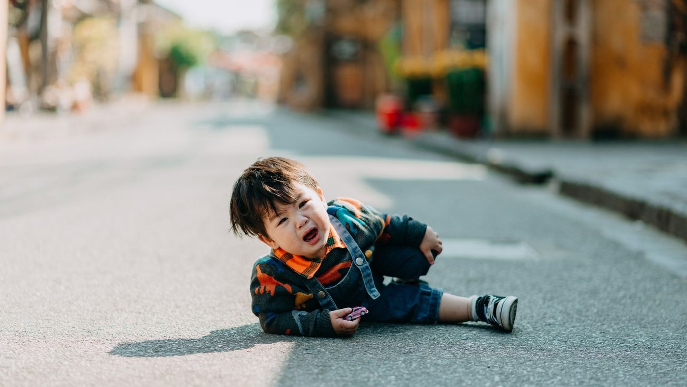 Jeune enfant en pleurs, assis au milieu d'une rue, en pleine crise de colère