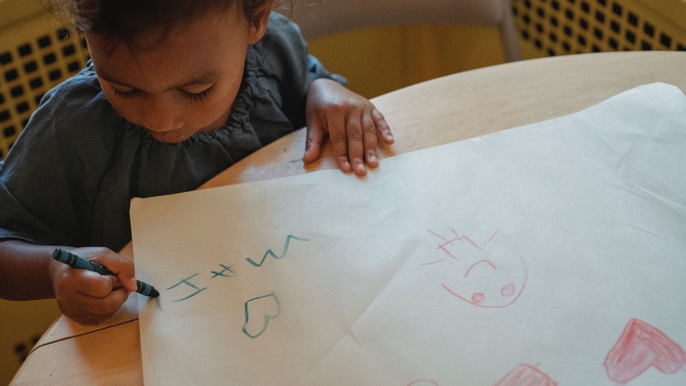 Un tout-petit dessine des cœurs et des traits sur une grande feuille posée sur la table