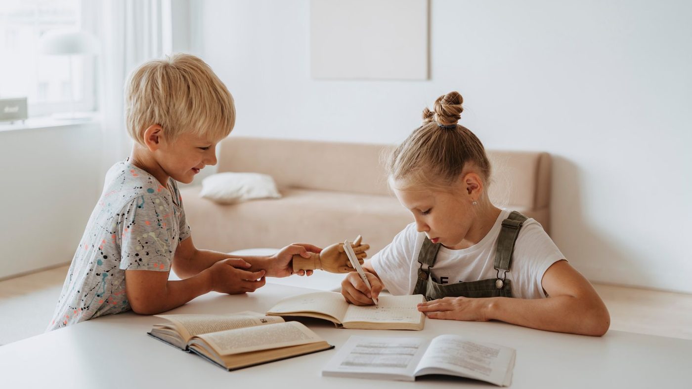 Deux enfants d'âges différents travaillent chacun sur leur livre à la même table