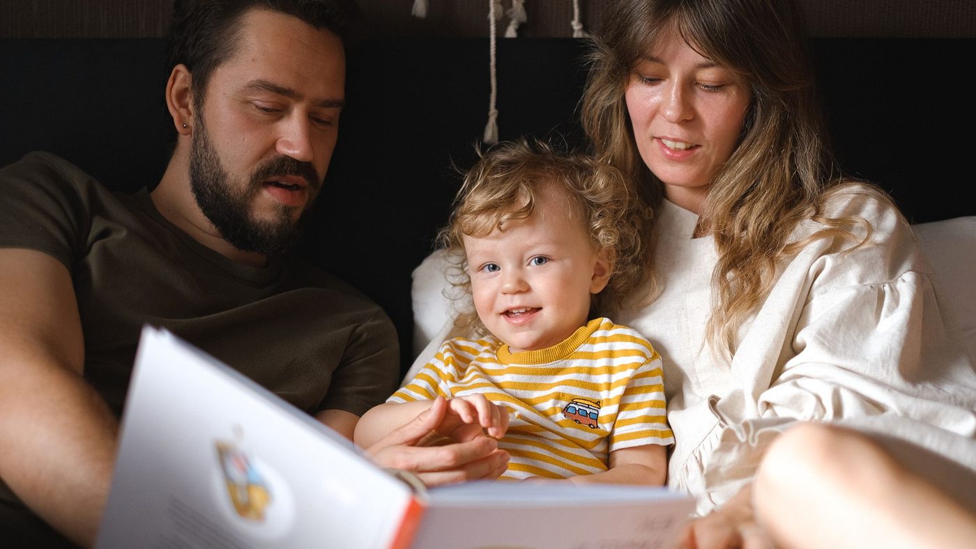 Un père et une mère lisent un livre d'images avec leur tout-petit, assis entre eux