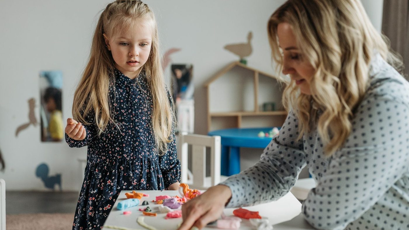 Une éducatrice assise à la table d'une enfant, penchée sur le travail en cours