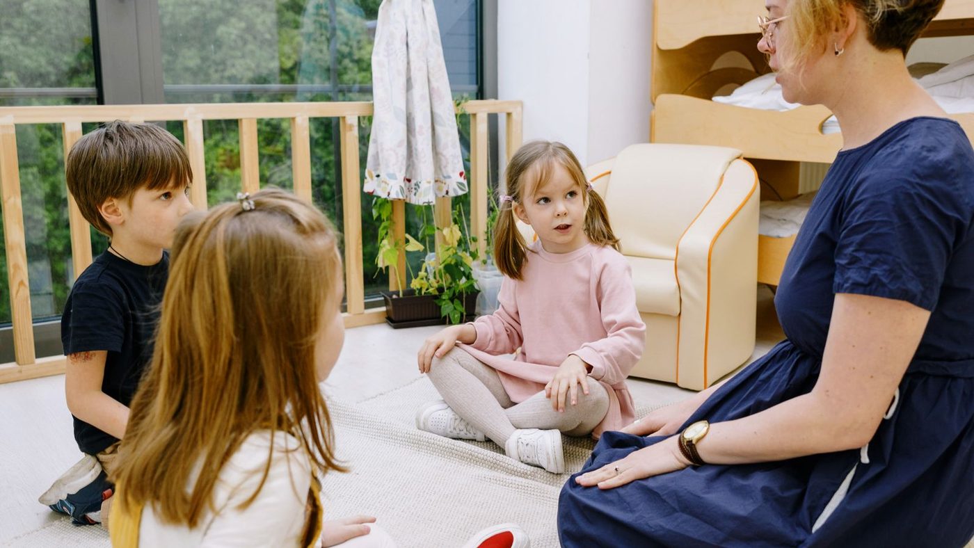 Éducatrice assise au sol, à hauteur de trois enfants, qui écoute