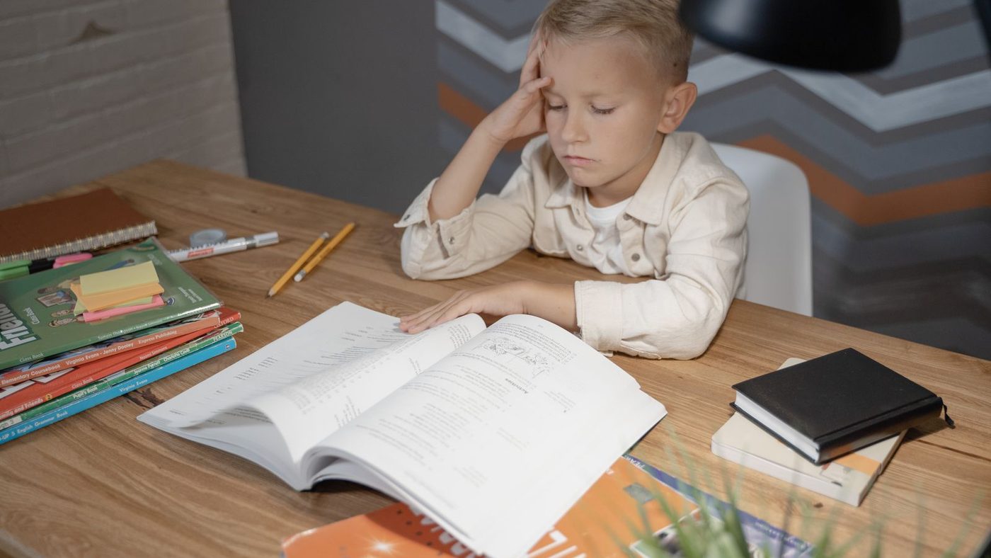 Un garçon la main sur le front, penché sur un livre ouvert, qui peine à lire