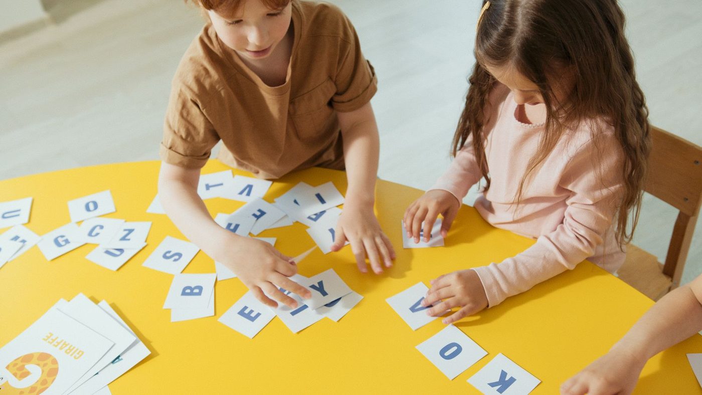 Deux enfants composent des mots avec des cartes de lettres sur une table