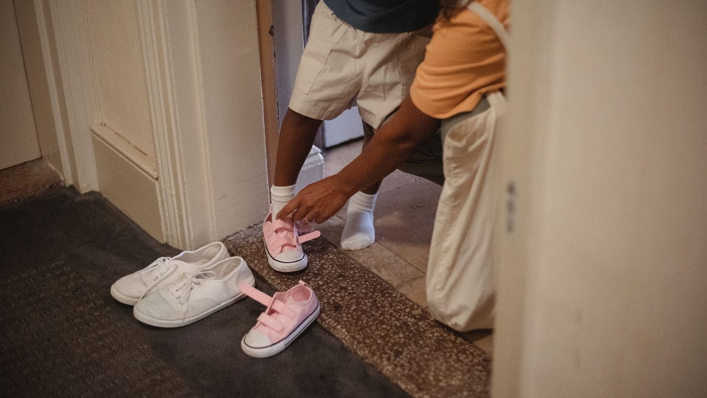 Dans l'entrée, un adulte aide un enfant à enfiler ses chaussures