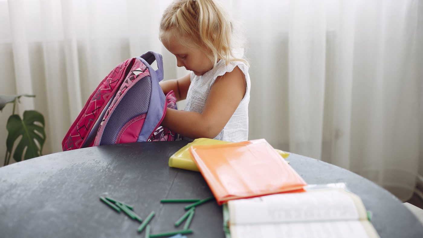 Une petite fille range ses affaires dans son cartable rose, posé sur la table