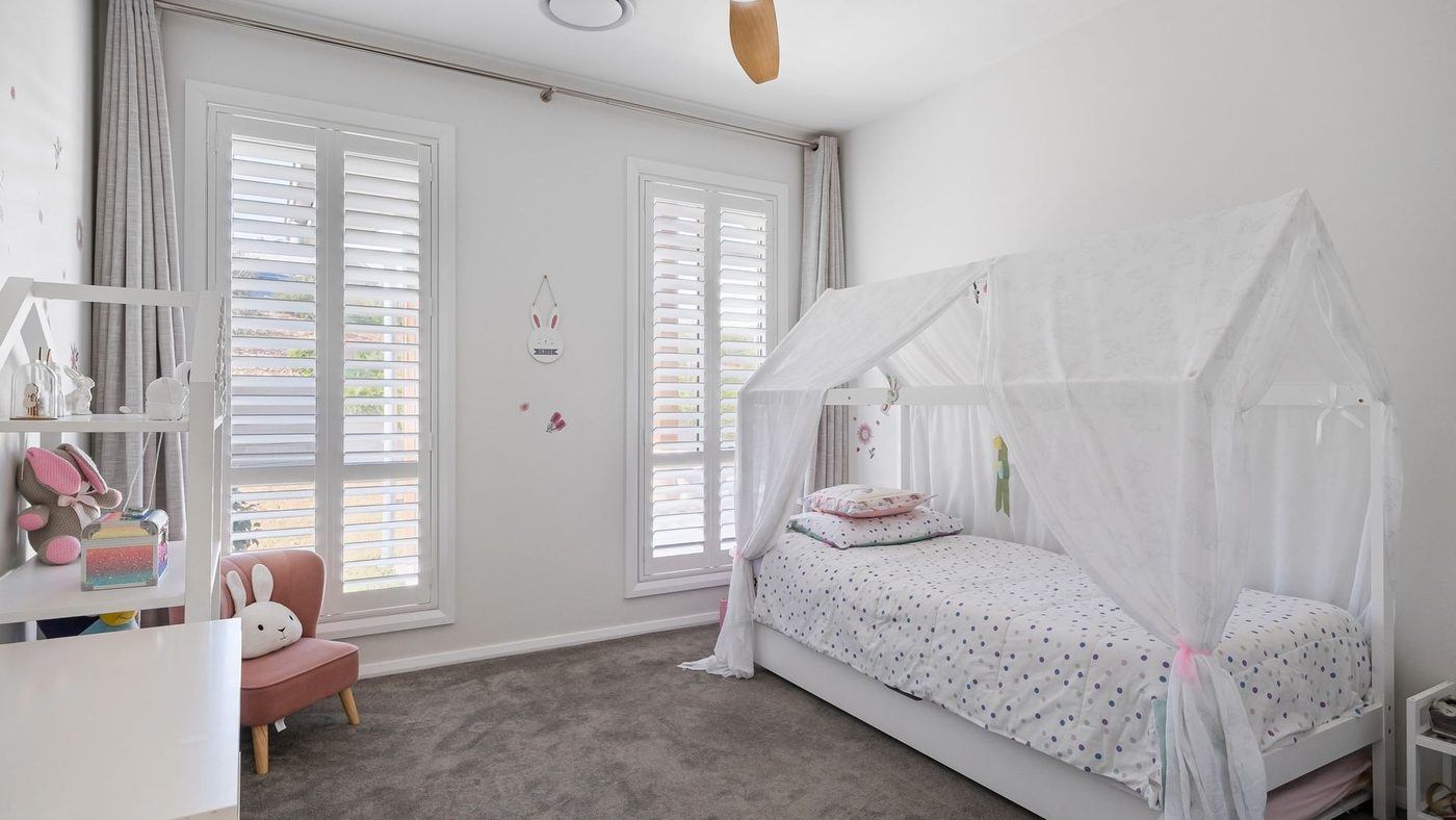 Un lit cabane bas avec un voile blanc dans une chambre d'enfant lumineuse