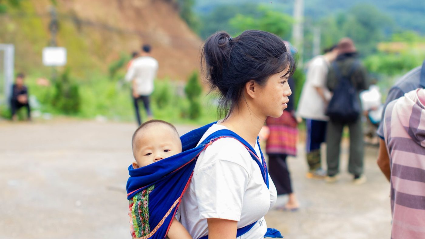 Une jeune femme porte son bébé sur le dos dans une écharpe bleue