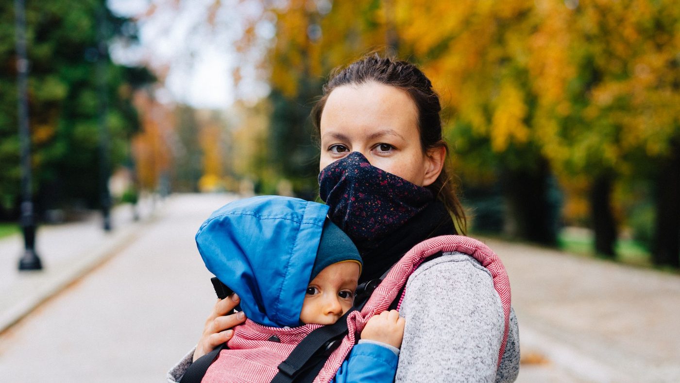 Une mère porte son bébé contre elle dans un porte-bébé, dans une allée en automne