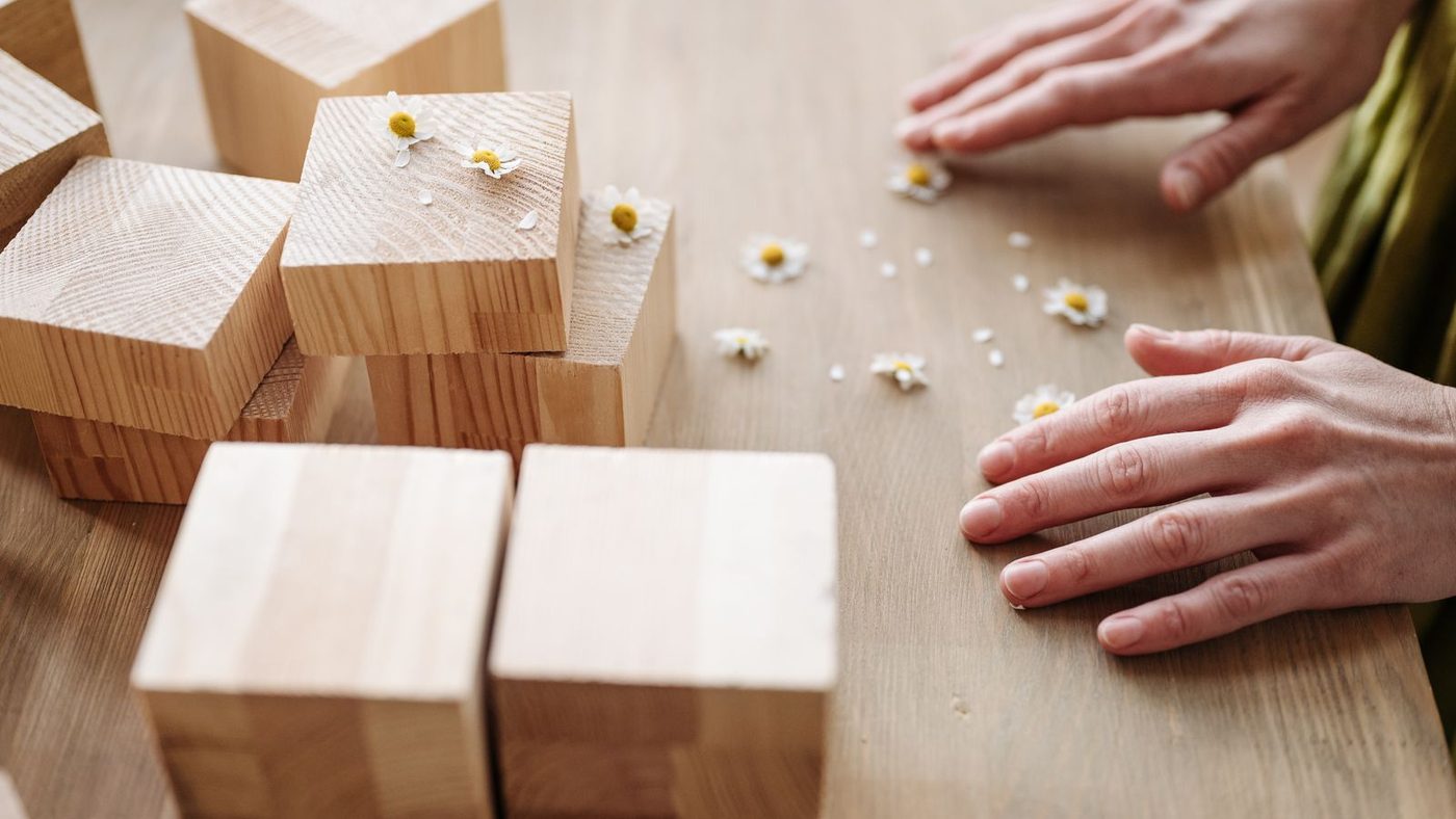 Les mains d'un adulte manipulent lentement des cubes de bois sur une table, sans rien d'autre autour