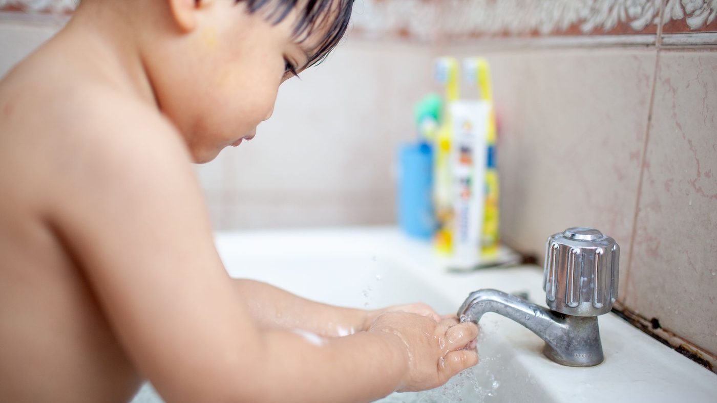 Un jeune enfant se lave les mains seul sous le robinet du lavabo
