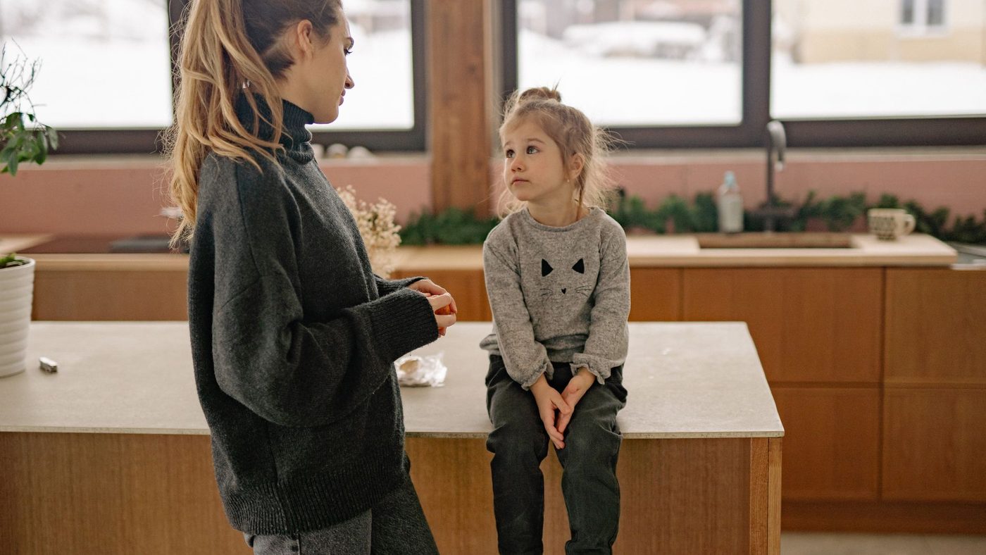Une mère parle à sa fille assise sur le plan de travail de la cuisine